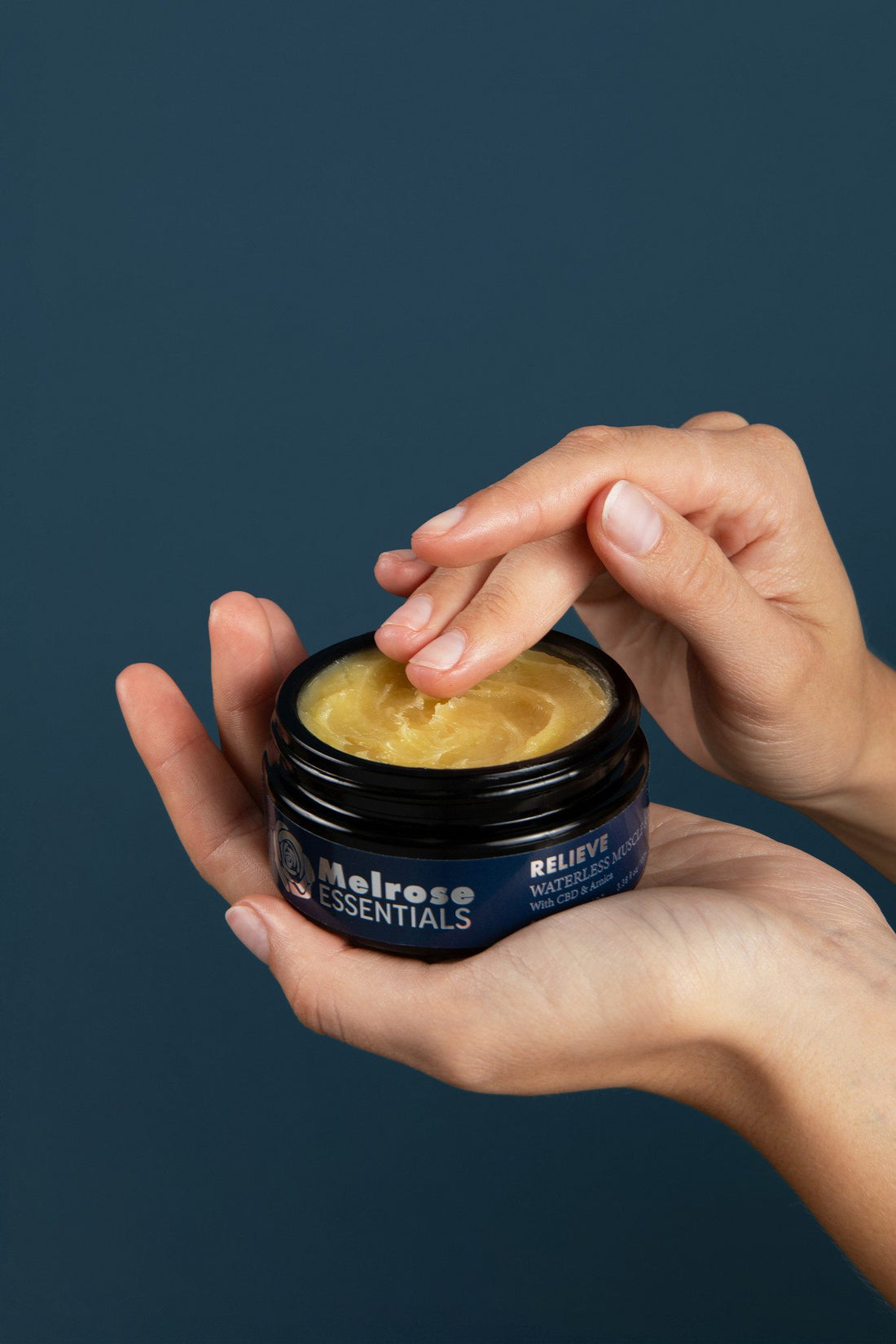 Hands taking Melrose Relieve waterless CBD cream from an open jar before a massage
