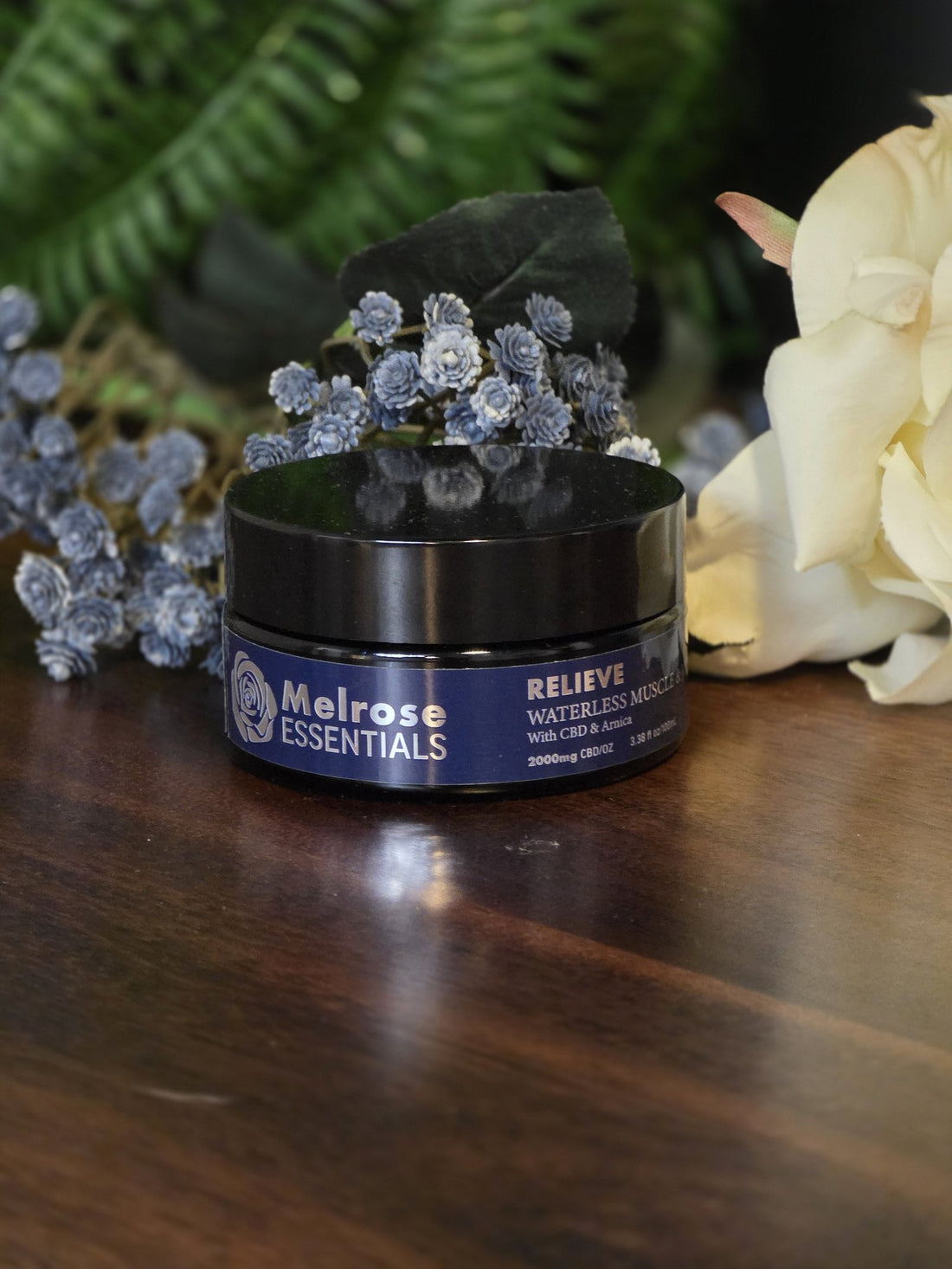 Melrose Relieve broad-spectrum waterless CBD balm jar, labeled 0% THC, on a wooden table with flowers