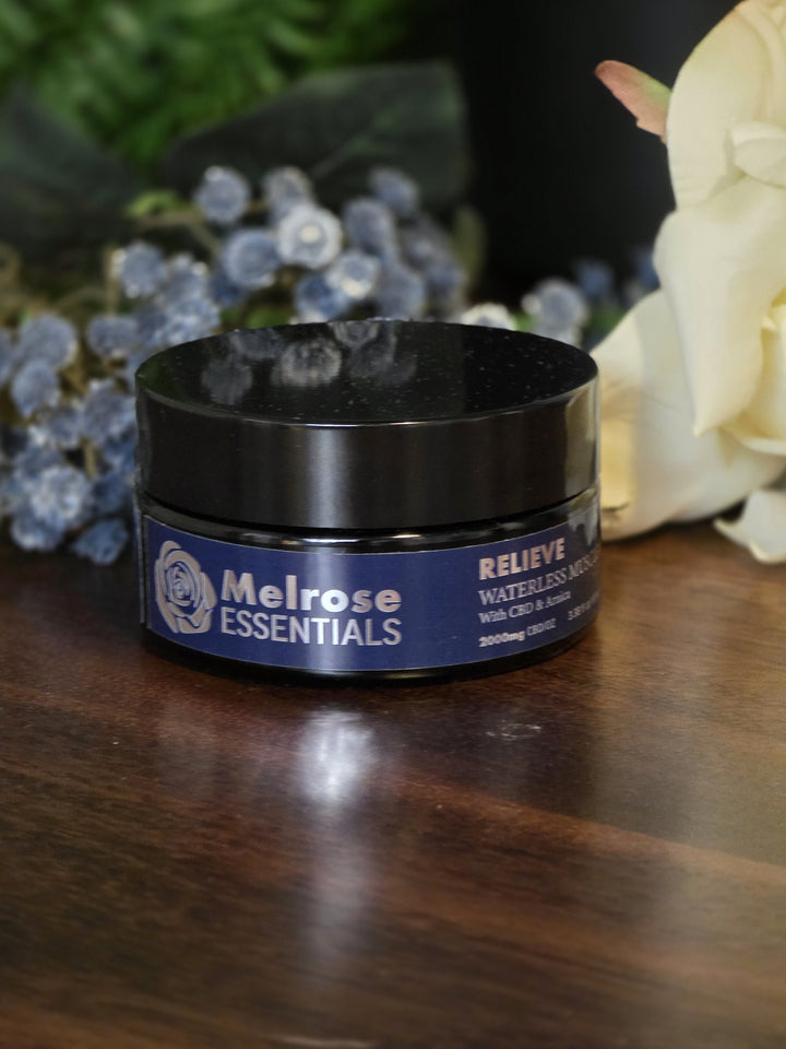 Melrose Relieve waterless CBD balm 100 ml jar on a wooden table with blue and cream flowers
