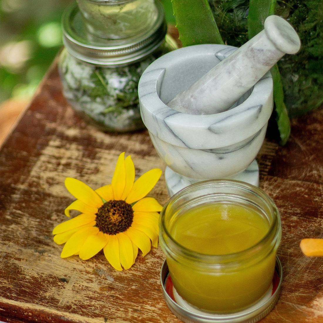 Mortar and pestle with a jar of Melrose Essentials Relieve CBD cream on a wooden surface next to herbs.