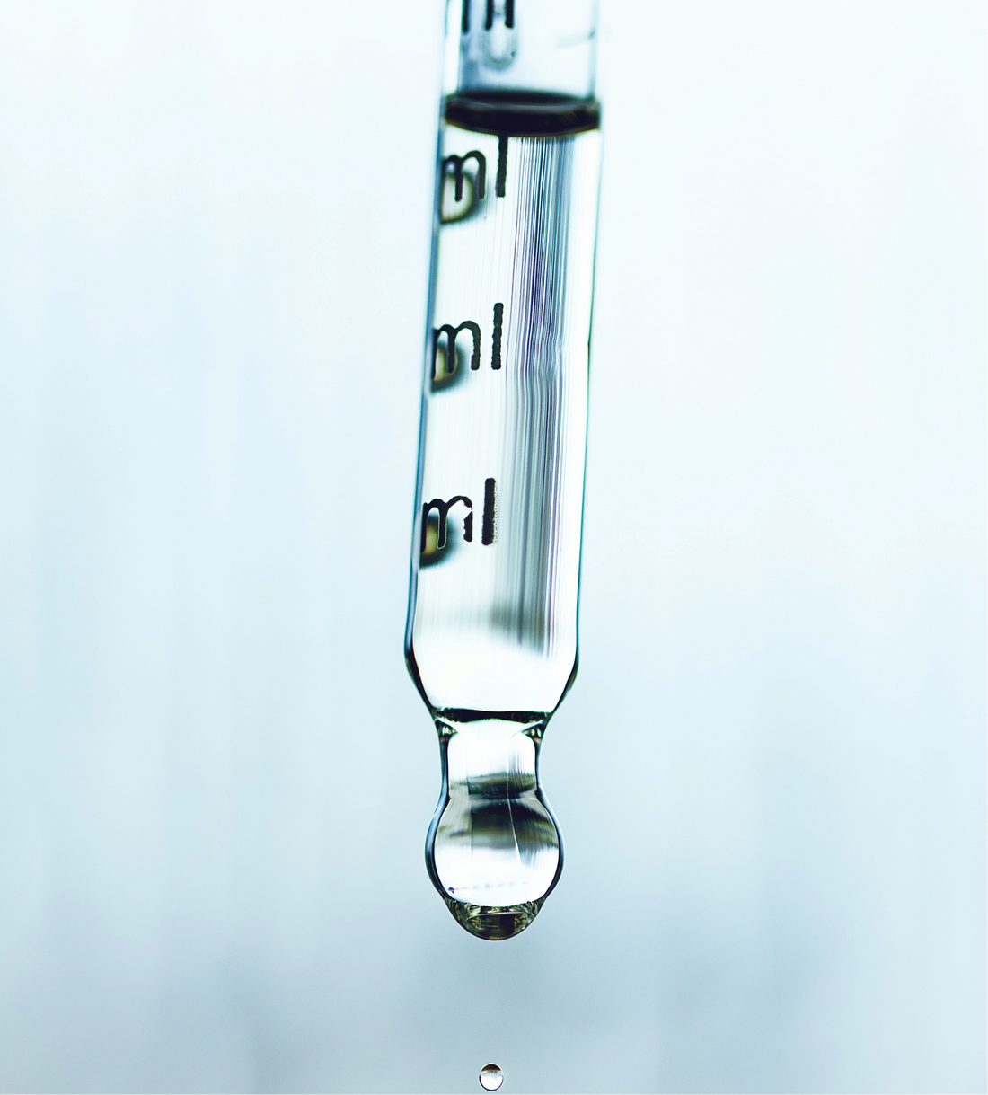 Glass dropper with liquid being dispensed on a light blue background