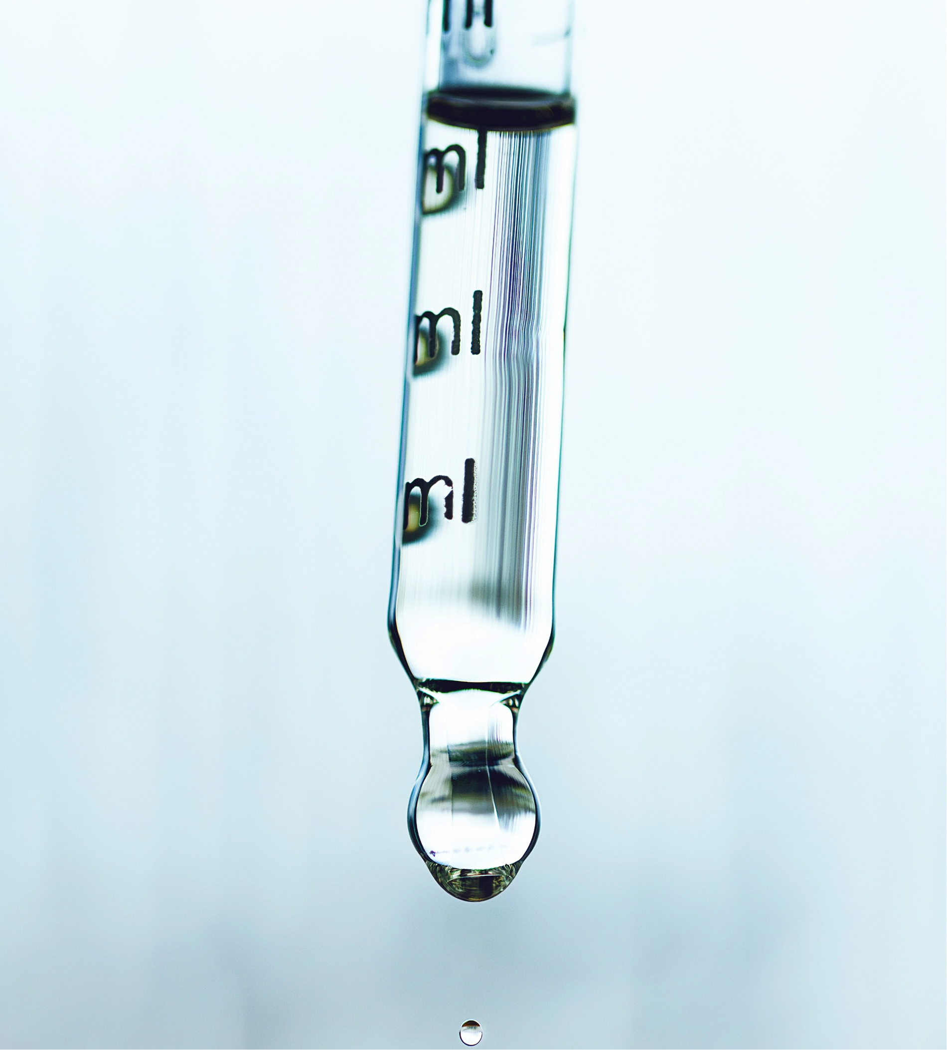 Glass dropper with liquid being dispensed on a light blue background