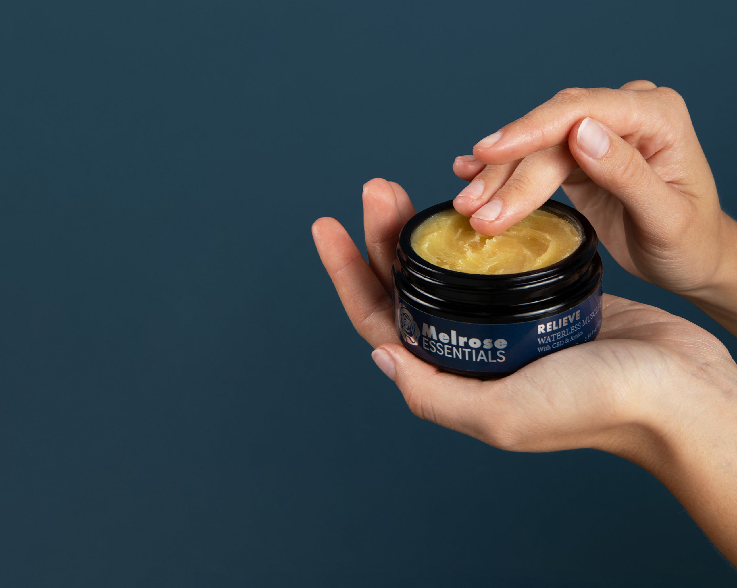 Hand holding a jar of Melrose Essentials Relieve CBD cream against a dark background