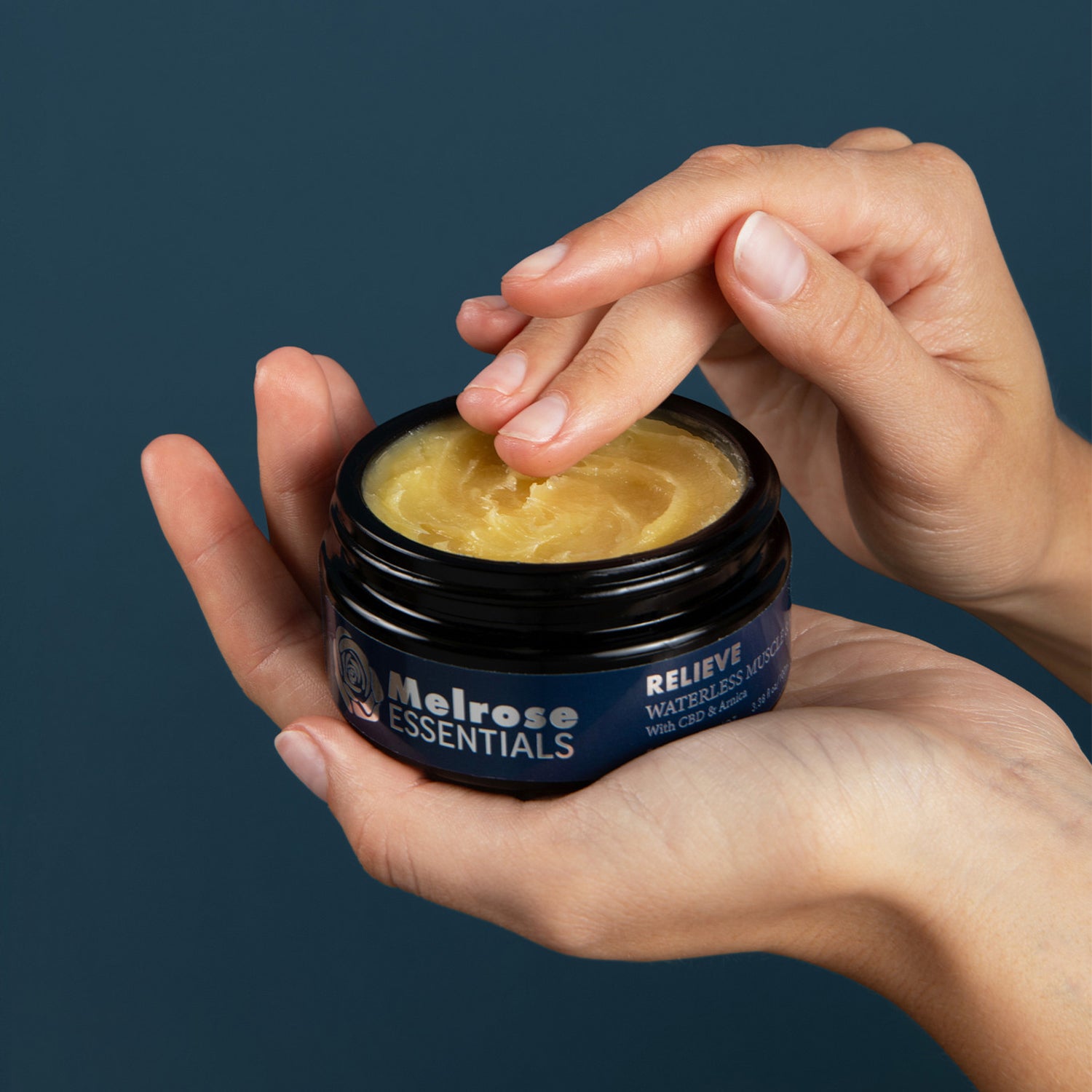 Person holding a jar of Melrose Essentials CBD cream with a dark background