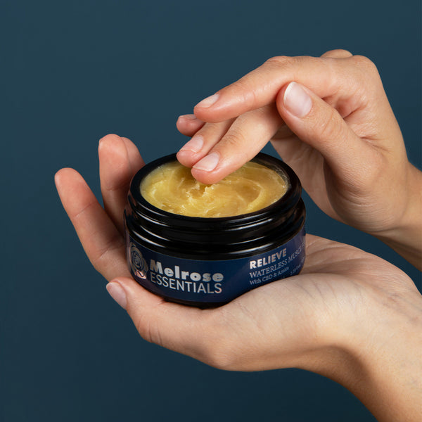 Person holding a jar of Melrose Essentials CBD cream with a dark background