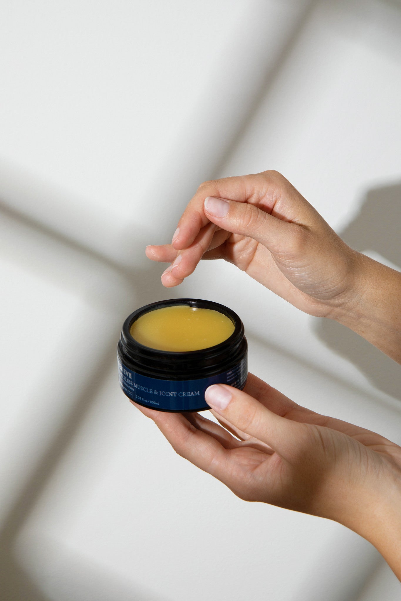 Hand holding a small jar of Melrose Essentials CBD cream against a neutral background