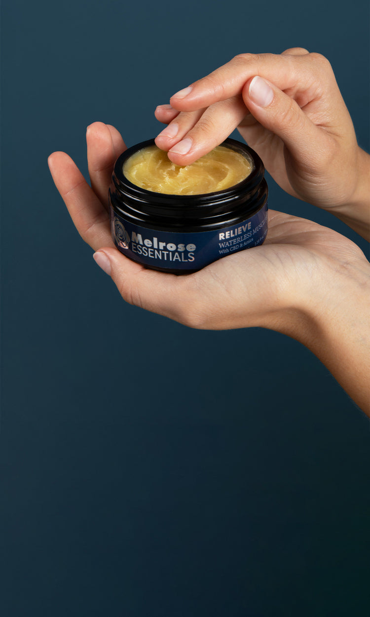 Hand holding a jar of Melrose Essentials Relieve cream against a dark background